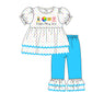 A children's two-piece outfit illustration featuring a white short-sleeve top with multicolored polka dots, a colorful chest graphic, and the words 'Adopt, Play, Love,' paired with bright blue pants with white polka-dot ruffled hems.